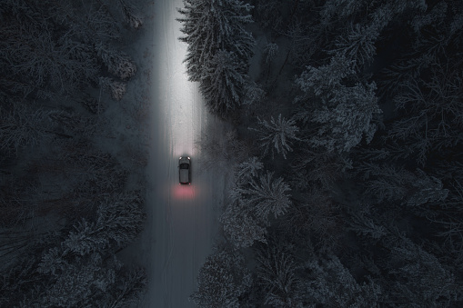 The car drives at night on a snowy forest road. Headlight illumination only. Air view. Vehicle topics