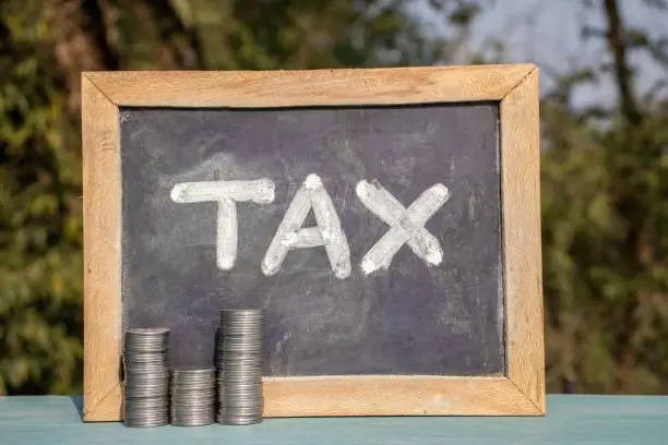 Tax Word Written on Chalk Board with Money Coin Stack in Horizontal Orientation.