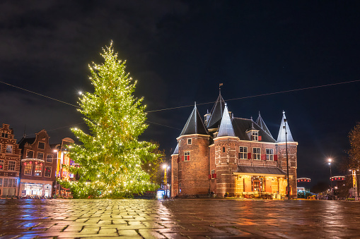 Amsterdam Christmas tree at the Waag building on the Newmarkt square with Christmas lights illuminating the pine tree in the evening.