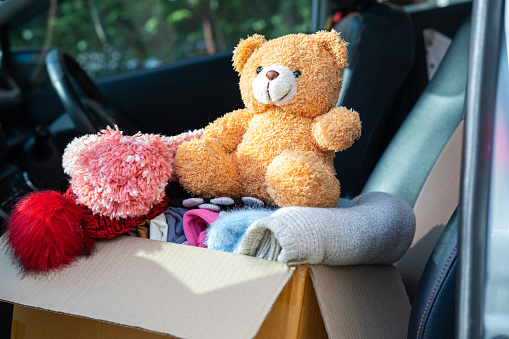 Volunteer woman provide clothing donation box with used clothes and doll at home to support help for refugee, homeless or poor people in the world.