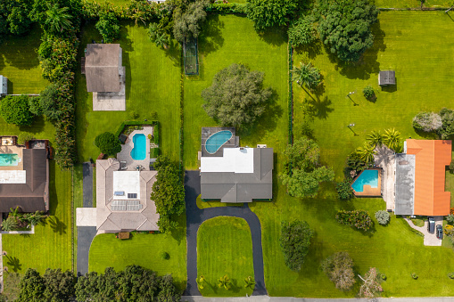 Aerial drone view of beautiful facade of a houses with tiles, with a park with short grass, trees and palms, blue sky, entrance