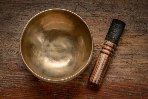 handmade Tibetan singing bowl with a mallet, top view against rustic wood, sound therapy for healing, relaxation and meditation