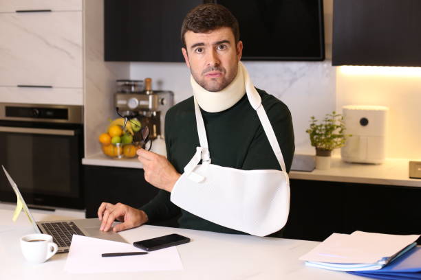 Worker doing home office after an accident A tired looking man in his forties is doing home office after an accident . He wears a cervical protective colla and an arm casket man with arm sling stock pictures, royalty-free photos & images