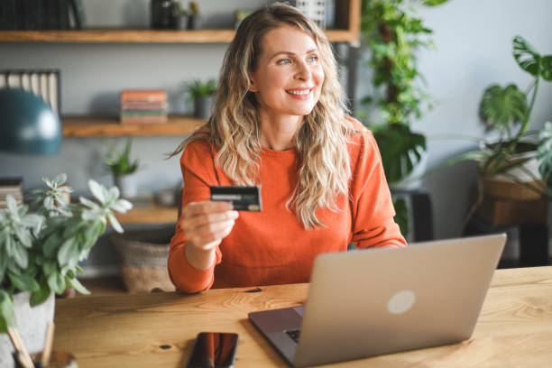 mujer adulta madura que trabaja en casa (computadora portátil, tarjeta de crédito) - credit card women laptop electronic banking fotografías e imágenes de stock