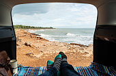 Personal perspective of feet in warm socks inside a camper van with the door open and views at a mediterranean coast.
