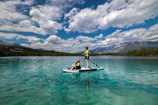 A Mother and son are paddleboarding on Edith Lake  in Jasper National Park, Alberta. The turquoise colored lake is very calm. Its is a beautiful sunny summer day in the Canadian Rockies.