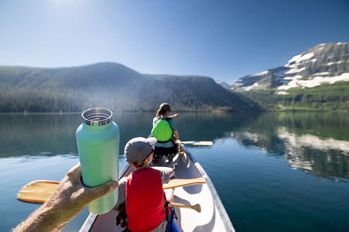 Family canoeing on Cameron Lake in Waterton Lakes National Park in the Canadian Rockies. They are spending time together and bonding. It is a beautify sunny summer day. The reflection of the mountains in the water is perfect. The father is holding a reusable water bottle.