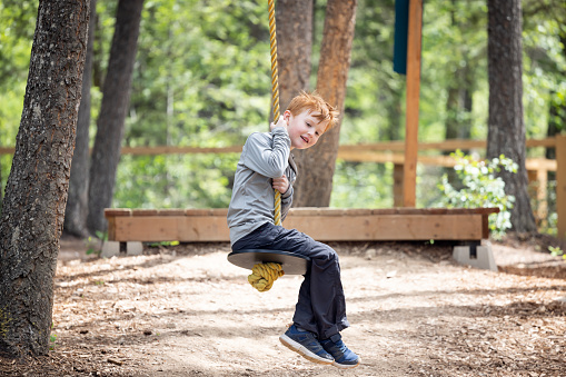 Positive little redhead boy ziplining at outdoor treetop adventure park being active and brave