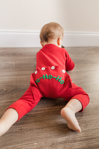 Un bebé navideño de 11 meses con 12 dedos de los pies vestido con pijamas navideños rojos de inspiración vintage con las palabras 