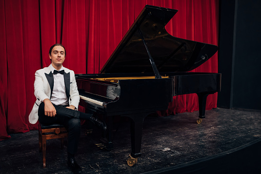 Portrait of a talented young man, sitting in a theater next to a piano and looking directly at the camera