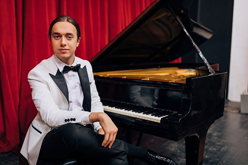 Front view of a young, talented man with long, tied hair sitting next to his piano and looking directly into the camera