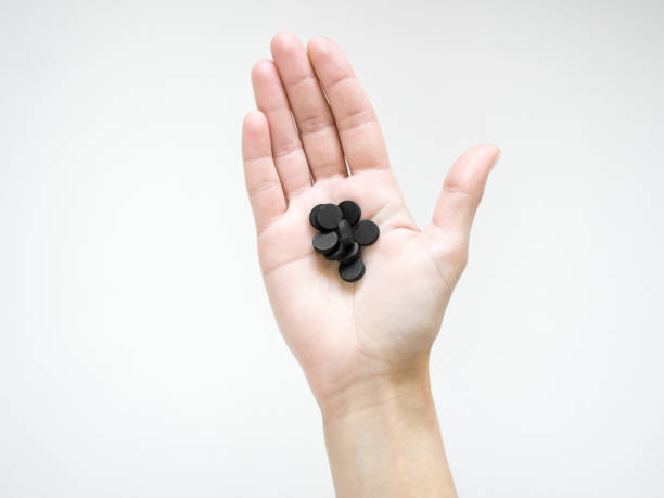 a woman holds a black sorbent pills. detox concept - medicated imagens e fotografias de stock