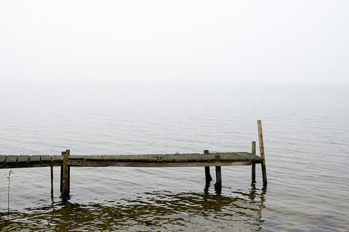 A rickety wooden jetty in December in the Veluwemeer between Gelderland and Flevoland. The horizon disappears in the morning fog.