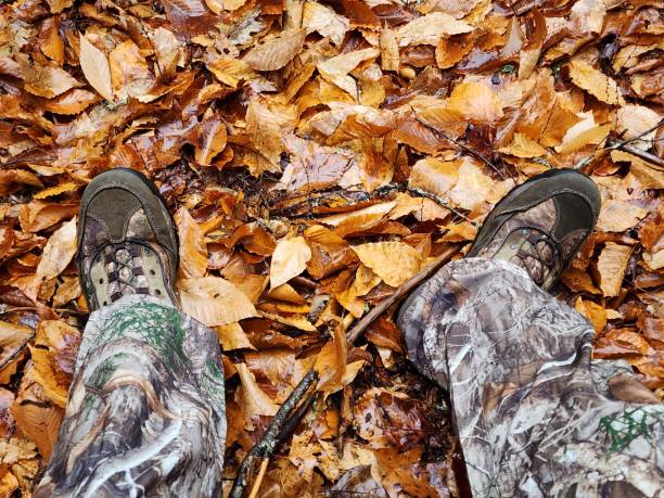 Hunter sitting in the woods during hunting season. Wearing camo boots and pants. Leaves on the ground.