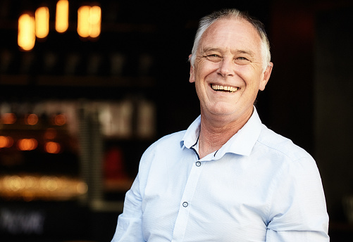 Man in his 50s, dressed in a smart shirt, looks very happy and proud as he stands in front of the dark interior of an entertainment venue.