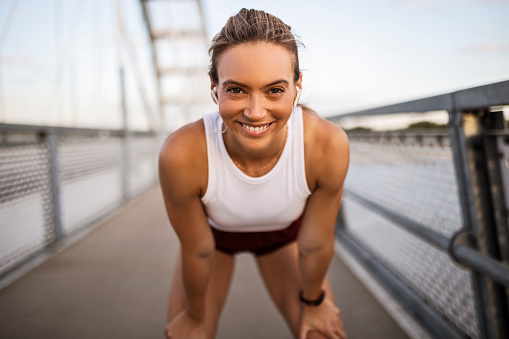 Young sportswoman taking a break after running on the bridge looking at camera smiling