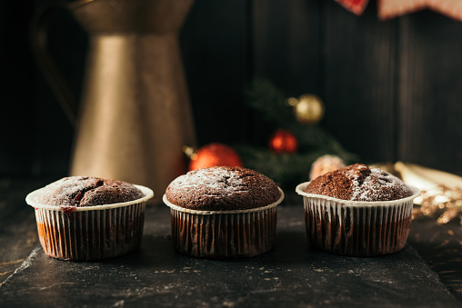 chocolate muffins with powdered sugar on top on a black background. Christmas decoration . Still life close up. Food photo.