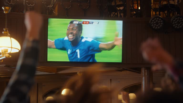 Friends Cheering for Their Soccer Team, Playing in an International Cup Final. Supportive Fans Standing in a Bar, Cheering, Raising Hands and Shouting. People Celebrate When Team Scores a Goal.