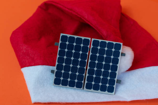 Santa Claus hat with photovoltaic solar panel and lamp isolated on orange background. Concept image. stock photo