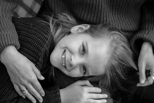 Black and white portrait of cheerful wonderful teenage girl child with long hair wearing sweater, lying on legs of woman mother caressing daughter, looking at camera. Childhood, relationship, autumn.