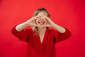 Portrait of happy woman with white snow smile in holiday red look with perfect bright makeup isolated on red background. Love expression, making heart shape by hands at face level. Healthy teeth
