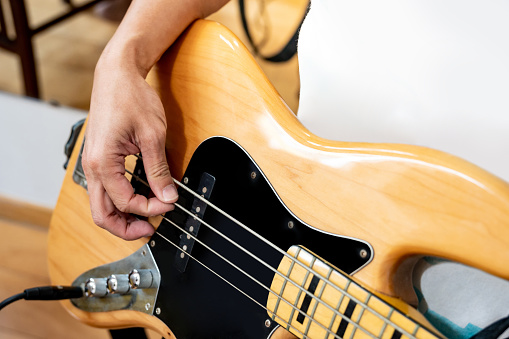 Bass guitar player or Bassist hand playing electric bass guitar in music recording studio. String instrument rehearsal for rock stage performance.