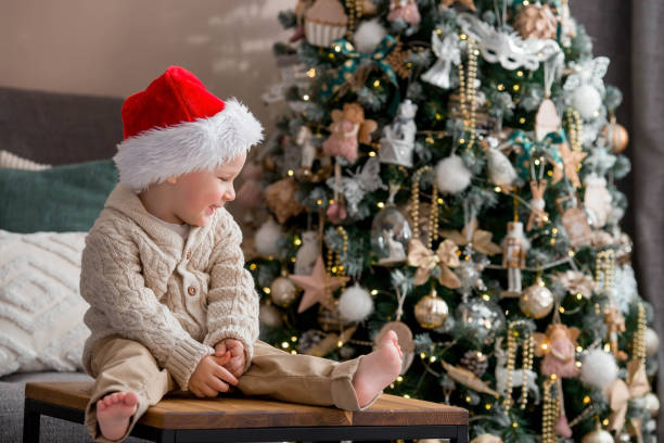 istock A beautiful little boy in a Santa Claus hat is sitting on a table and laughing merrily against the background of a Christmas tree and beautiful bokeh. The concept of celebrating Christmas. 1447762000