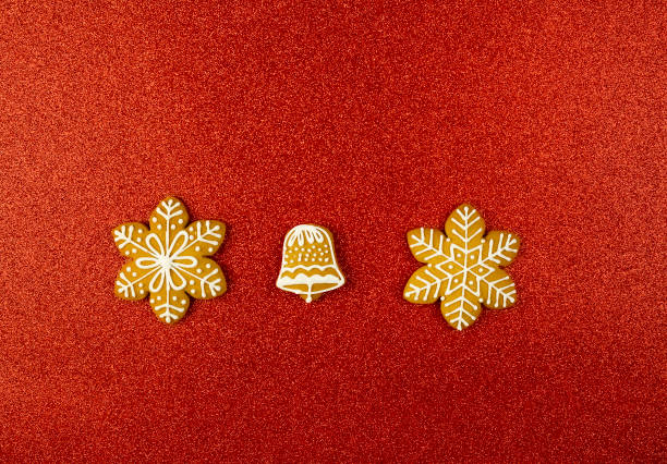 Snowflakes and bell on a red background. Gingerbread cookies decorated with icing on a red glitter background. Christmas glitter background.