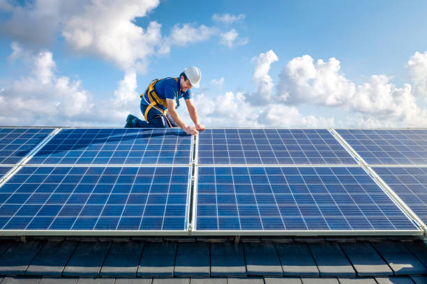 Professional worker installing solar panels on the roof of a house Male engineer in blue suit and protective helmet installing photovoltaic panel system. Professional electrician mounting solar module on roof. Alternative energy ecological concept rooftop solar stock pictures, royalty-free photos & images