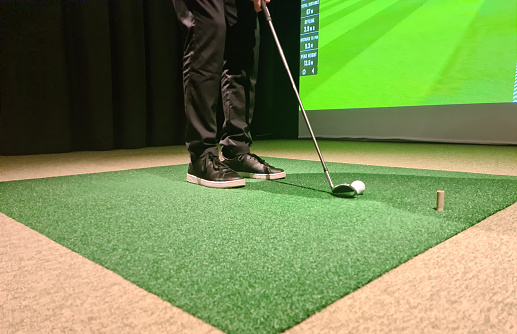 Man is playing golf on golf simulator and getting ready to hit. Screen means information about swing and range of impact