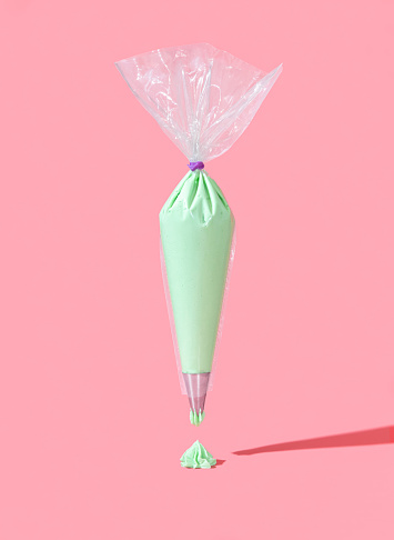 Pastry bag full of green buttercream frosting, minimalist on a pink background. Flying frosting bag in bright light on a colorful table.