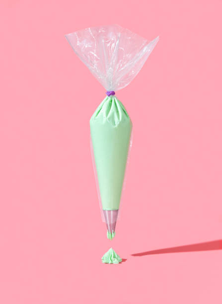 Frosting bag isolated on a pink background. Green buttercream icing in a plastic bag stock photo