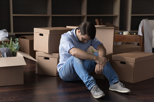 Upset frustrated man sit on floor near heap of stacked cardboard boxes with stuff feels depressed, having financial problems, leaves house due to bank debt, suffers from eviction, bankruptcy, divorce