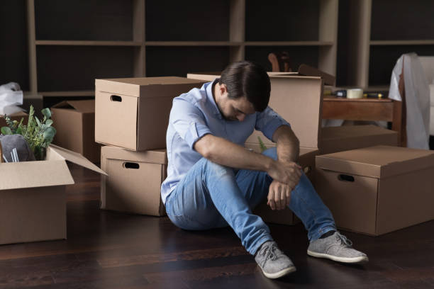 Upset man sit on floor near heap of cardboard boxes Upset frustrated man sit on floor near heap of stacked cardboard boxes with stuff feels depressed, having financial problems, leaves house due to bank debt, suffers from eviction, bankruptcy, divorce belongings stock pictures, royalty-free photos & images