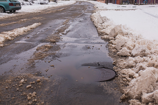 Puddle on asphalt. Road with snow sprinkled with sand. Winter background. Weather. Climate