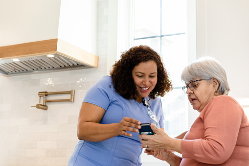 The senior adult woman asks her nurse for help to look up the pharmacy information on her phone.