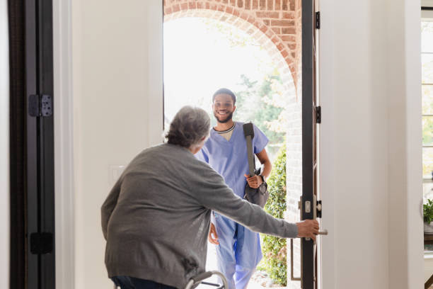 Senior man with walker opens door for physical therapist stock photo