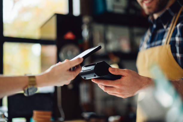 Anonymous Person Paying With Their Cell Phone Unrecognizable people making an online payment. Anonymous man is holding a card machine while the other person is placing their phone to pay. point of sale stock pictures, royalty-free photos & images