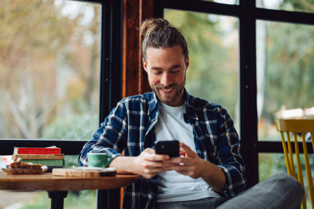 istock Handsome Smiling Man Sitting in a Cafe and Texting on His Phone 1447777473