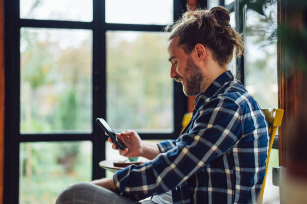istock Handsome Smiling Man Sitting in a Cafe and Texting on His Phone 1447777499