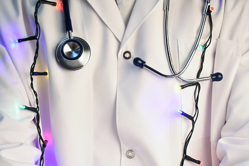 Happy and healthy new year. Doctor wishes you a happy new year. Stethoscope and Christmas lights around the his neck