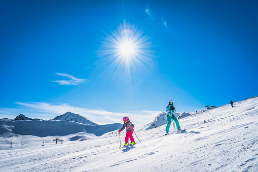 Mother teaching daughter how to ski, skiing down on a ski slope. Sunny day on ski winter holidays in Andorra, El Tarter, Pyrenees Mountains