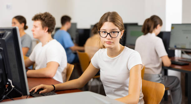 istock Positive female teenager in glasses learning computer science while she is using a PC in the computer classroom 1447781621