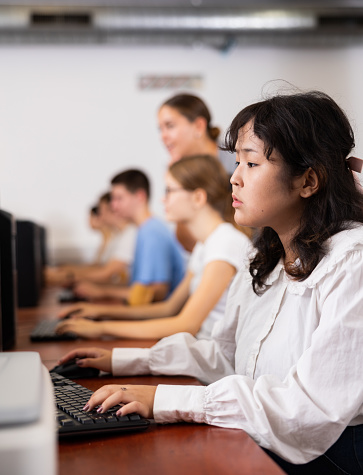 Focused asian teenager female student sitting in computer class with pc, preparing for exam