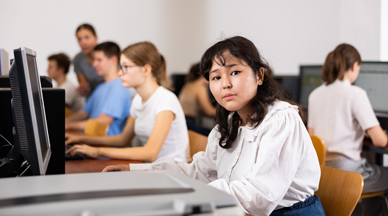 Portrait of fifteen-year-old schoolgirl studying at computer in a class at an informatics lesson with classmates