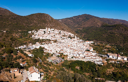 View from drone of picturesque Spanish town of Ojen in green valley surrounded by Sierra Blanca and Sierra Alpujata mountan ranges on sunny fall day, Malaga province
