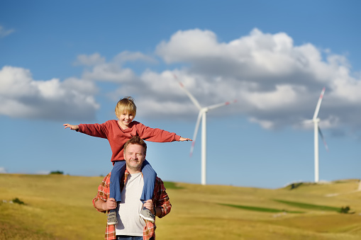 Eco activists man and child on background of power stations for renewable electric energy production. People and windmills. Wind turbines for generation electricity. Green energy concept