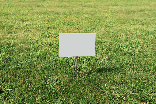 Blank information sign board mounted on lawn green grass in city park outside