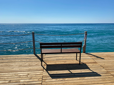 A wooden bench on the pier on the embankment against the backdrop of the sea on vacation in a heavenly warm eastern tropical country resort.