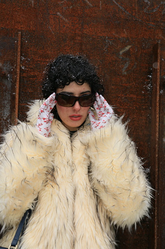 A Colombian model outdoors in autumn during a snow storm. She is wearing sunglasses, white pattern gloves, white gloves and make up.